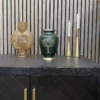 A brass cremation urn with a green finish and a tree carved in the middle